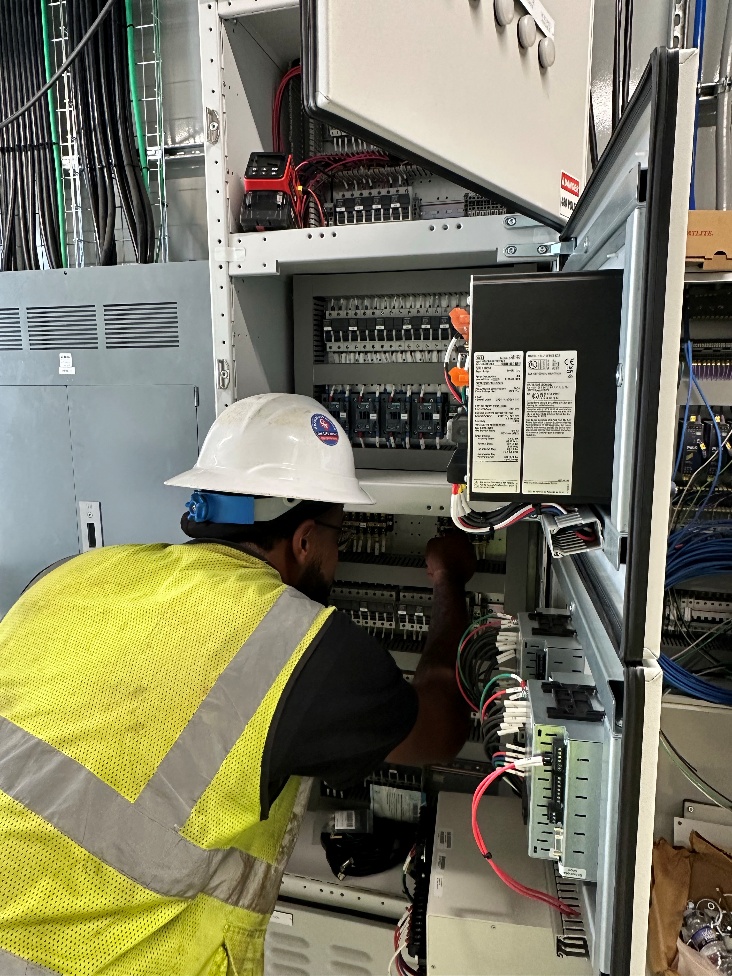 A technician traces wiring inside an electrical control cabinet.